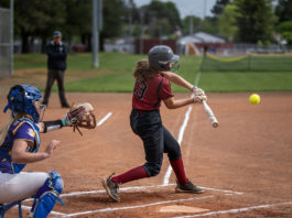 Girl hitting softball with catcher behind her