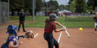 Girl hitting softball with catcher behind her