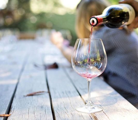 Traditional vs. Digital Marketing for Wineries and Vineyards Someone pouring a glass of red wine into stemware.