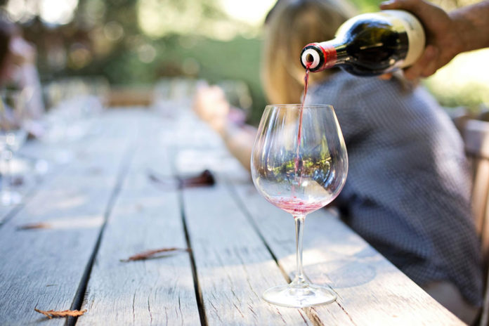 Someone pouring a glass of red wine into stemware.